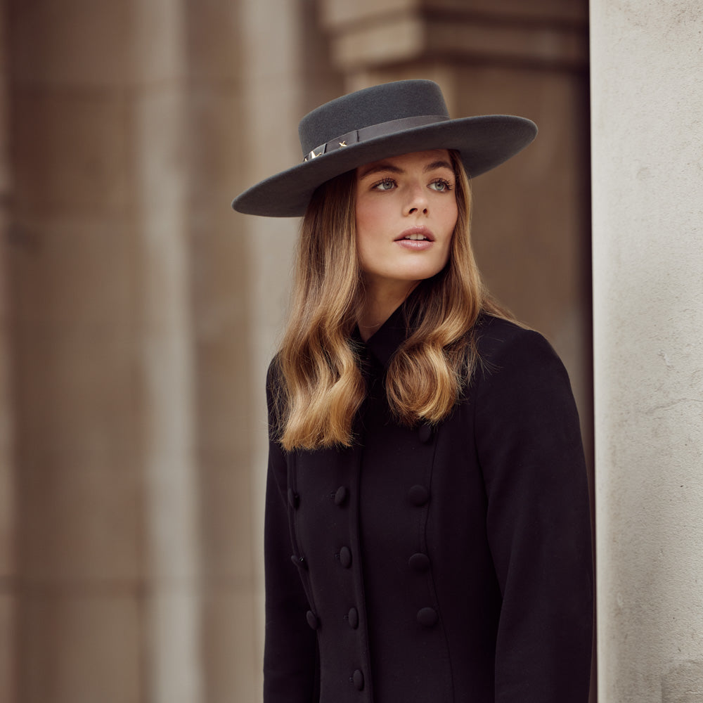 Woman with long hair wearing a black coat and a grey wool fedora and gold stars