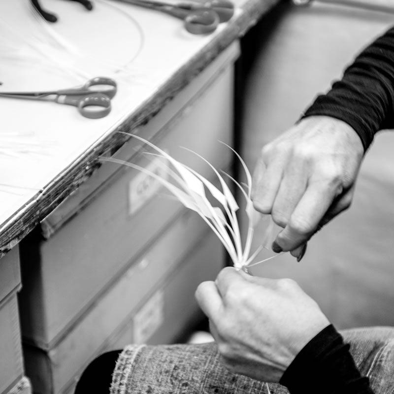 Two hands binding feathers together in a workroom