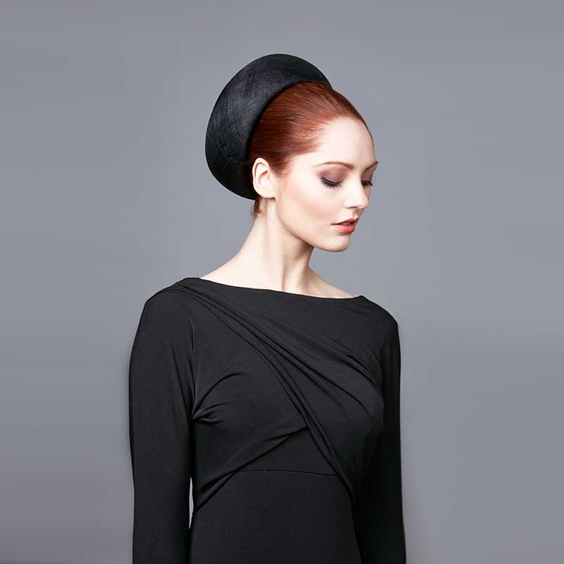 Woman with red hair wearing a black dress and a black fine straw Jackie O pillbox