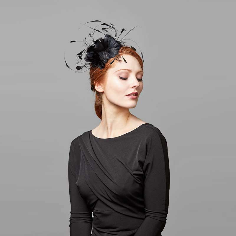 Woman with red hair wearing a black top and a black feather flower headband