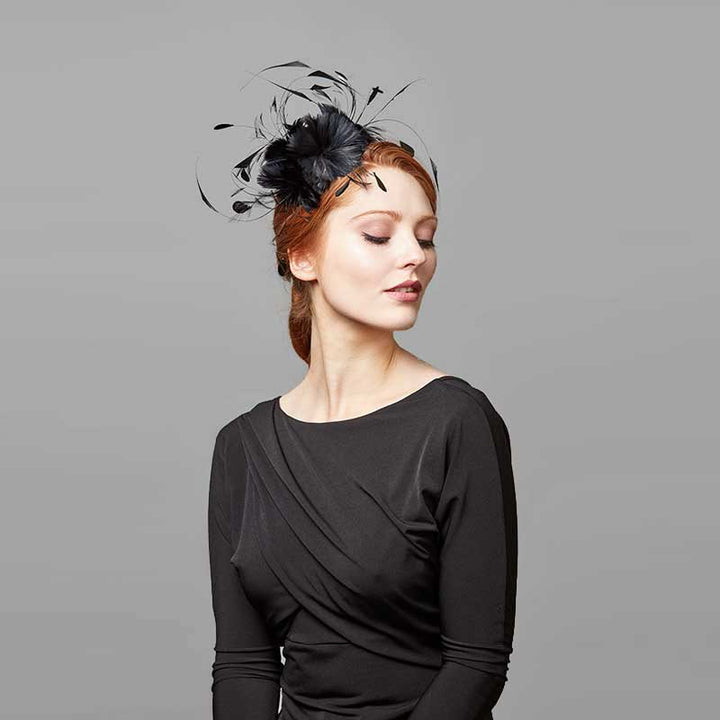 Woman with red hair wearing a black top and a black feather flower headband