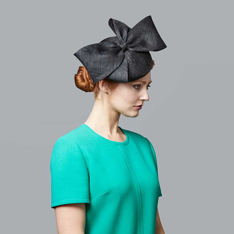 Woman with red hair wearing a green dress and a black straw pillbox with bow