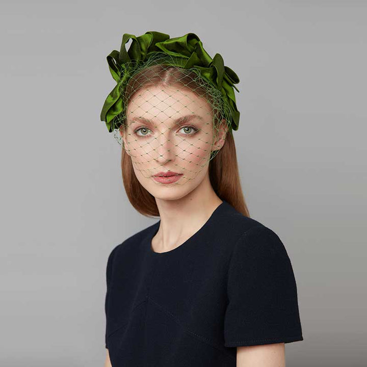 Woman with brown hair wearing a black dress and a green silk bow headband with face veil