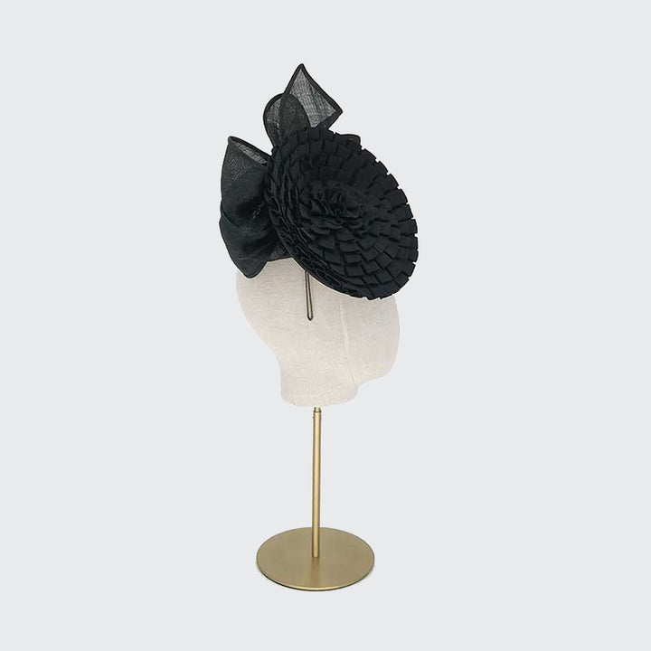 Side view of a black pleated grosgrain disc with a bow on a linen display head