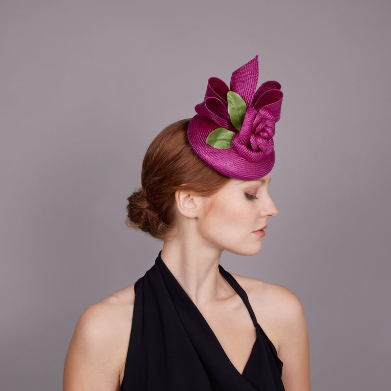 Woman wearing a black dress and a magenta straw pillbox with magenta straw camellia with a bow