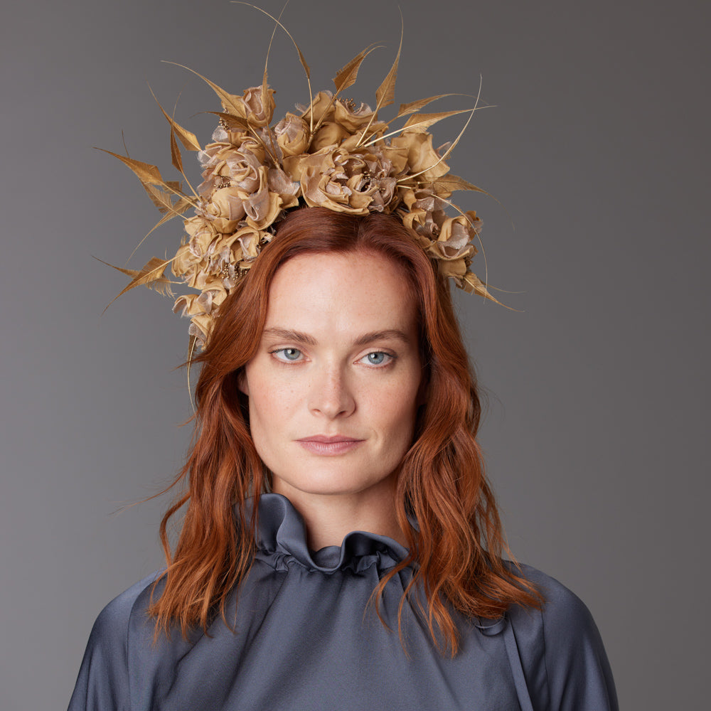 Woman with red hair wearing a grey blouse and a brass gold silk headdress with diamond-cut feathers