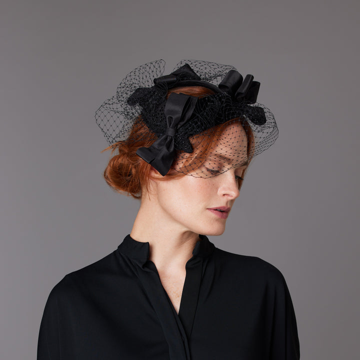 Woman with red hair wearing a black top and a silk trio of bows headpiece with veiling
