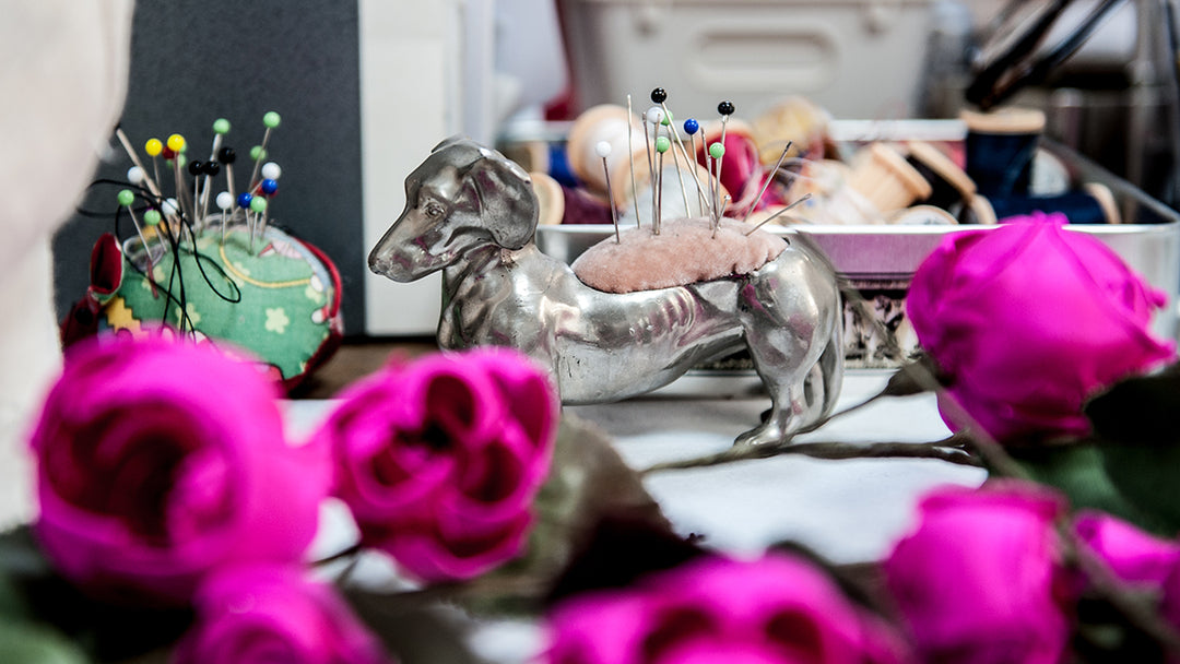 Work table with metal dog pin cushion, hot pink silk roses and another pin cushion