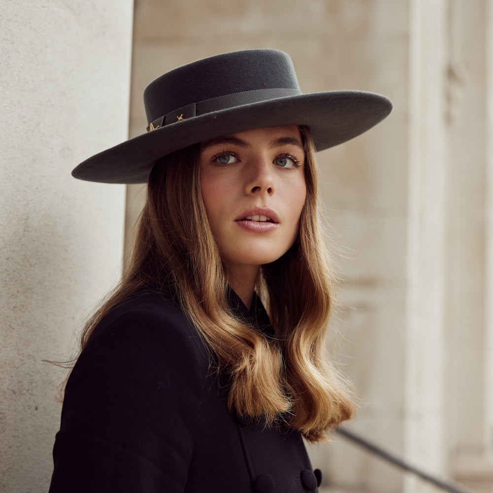 Woman with long hair wearing a black coat and a grey wool fedora and gold stars
