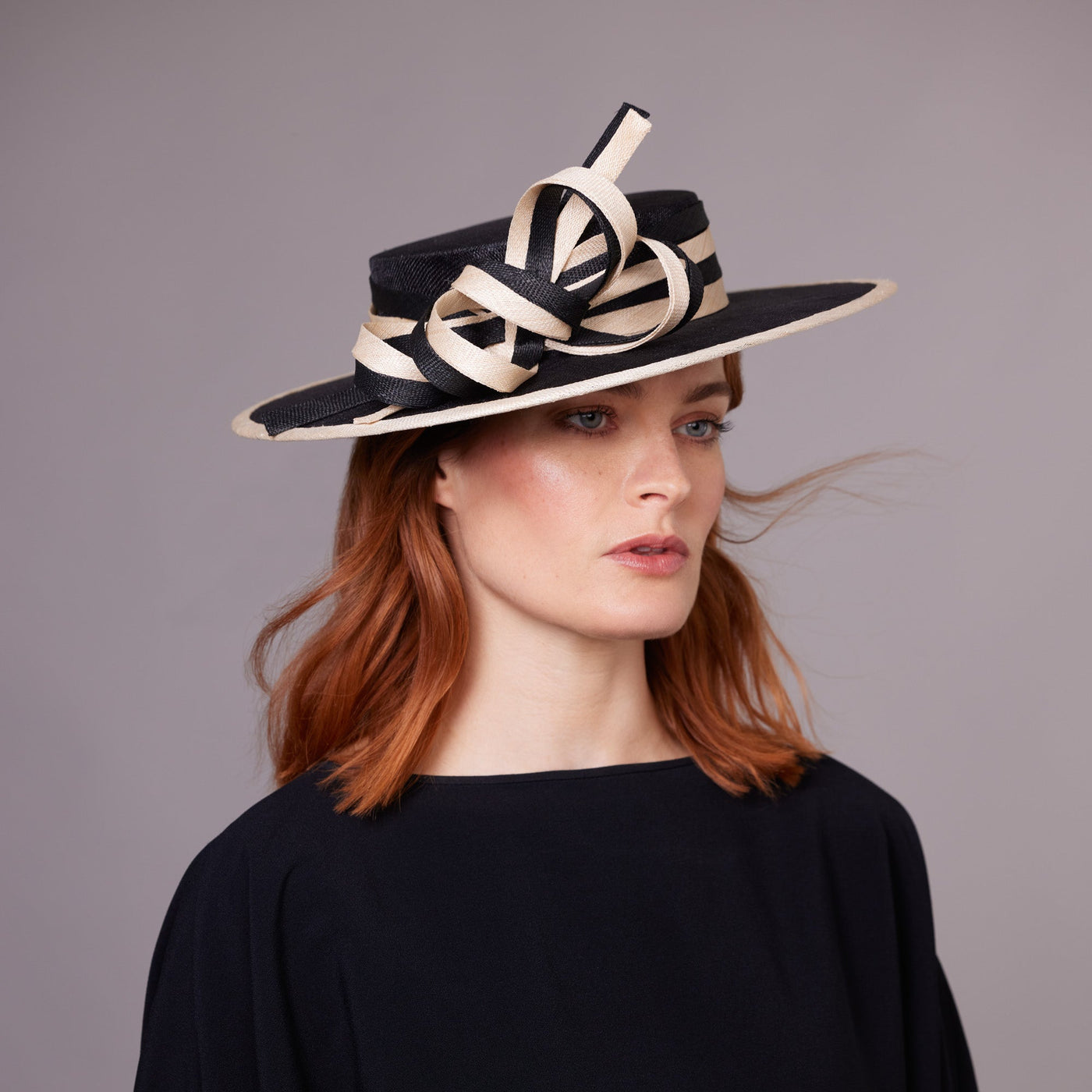 Woman with red hair wearing a black dress and a black boater with a natural edge and a striped band and bow