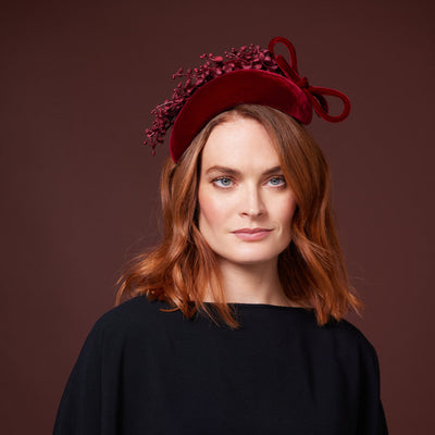Woman with red hair wearing a black top and a red velvet crescent with lily of the valley
