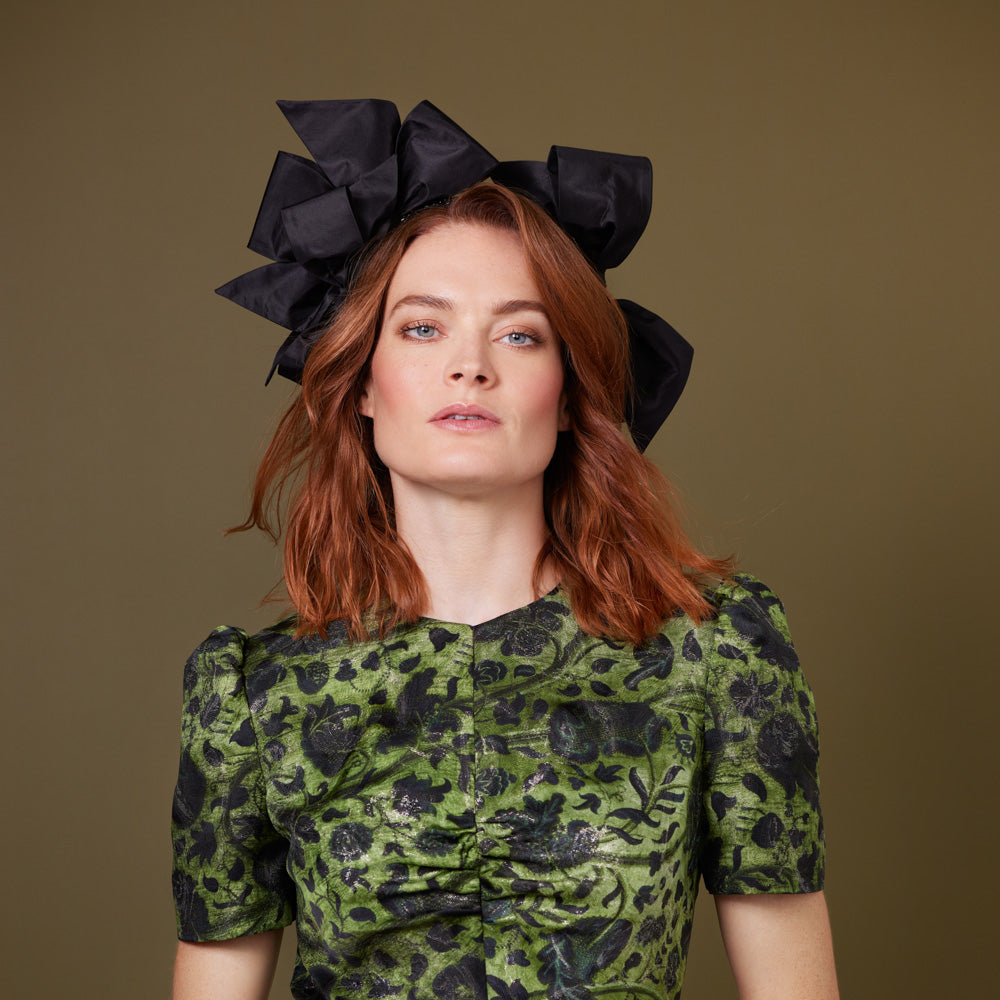 Woman with red hair wearing a green dress and a black beaded headband with bows