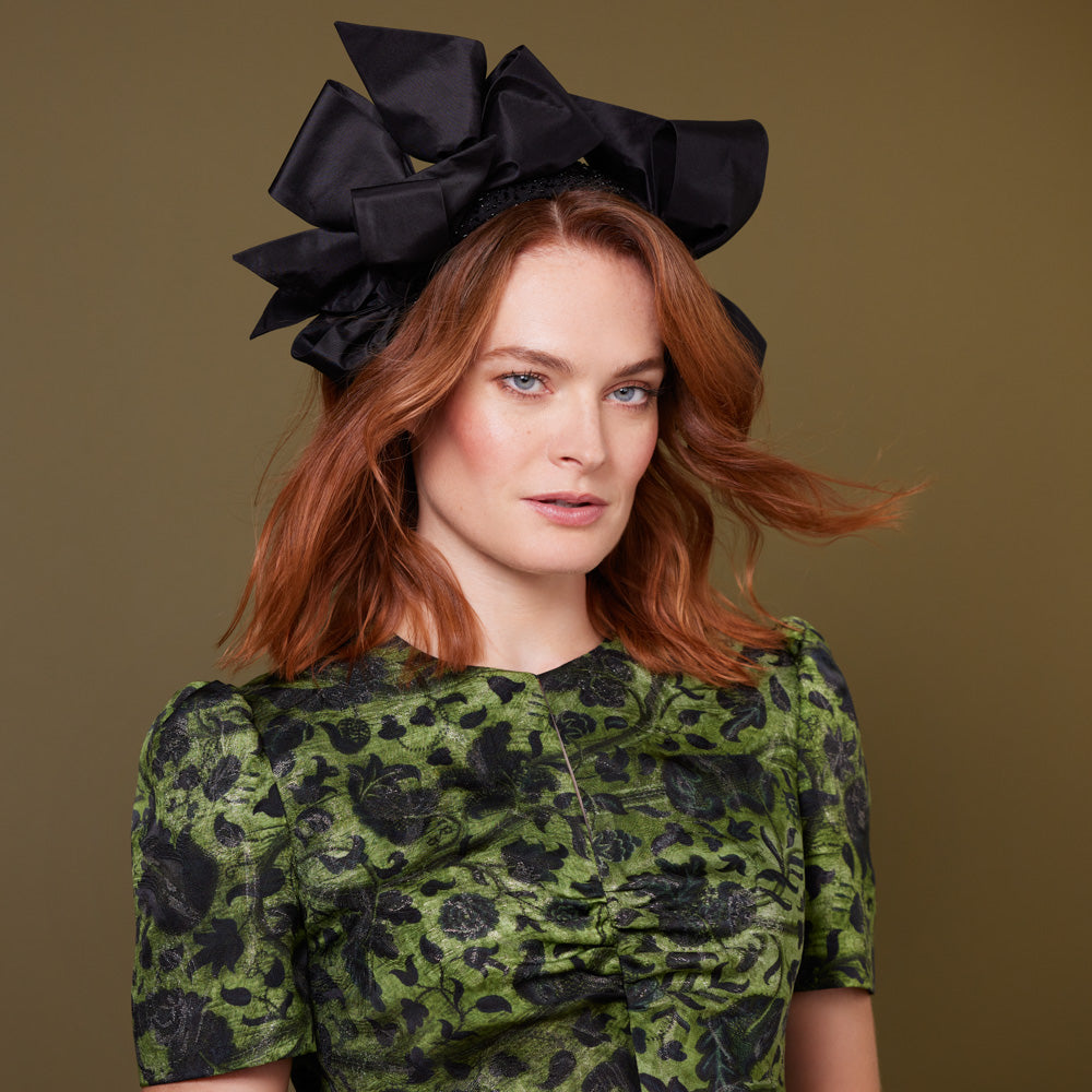 Woman with red hair wearing a green dress and a black beaded headband with bows