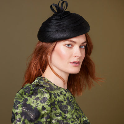 Woman with red hair wearing a green dress and a black fine straw beret with a twist