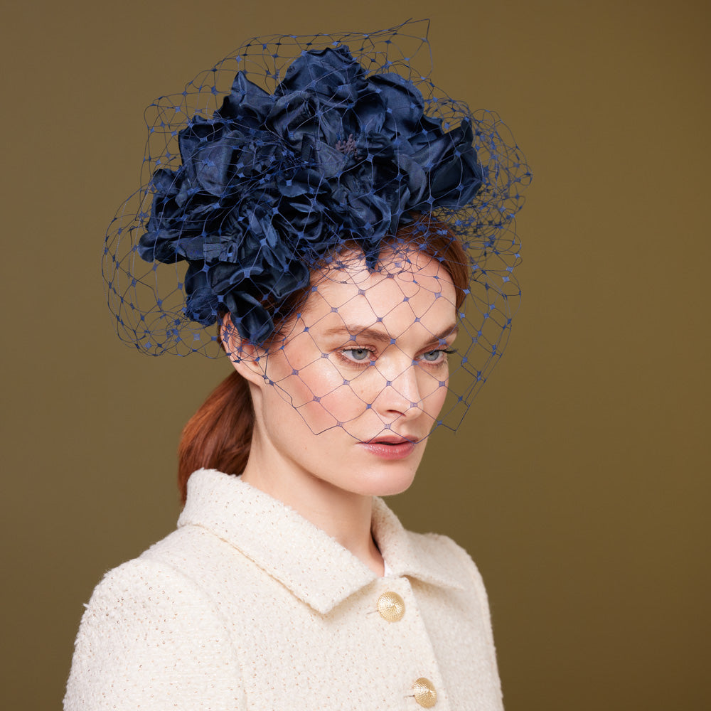 Woman with red hair wearing a light dress and a navy silk flower headdress with veiling
