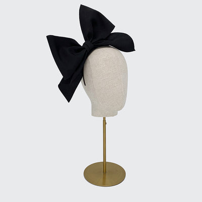 Side view of a black grosgrain bow headband on a linen display head