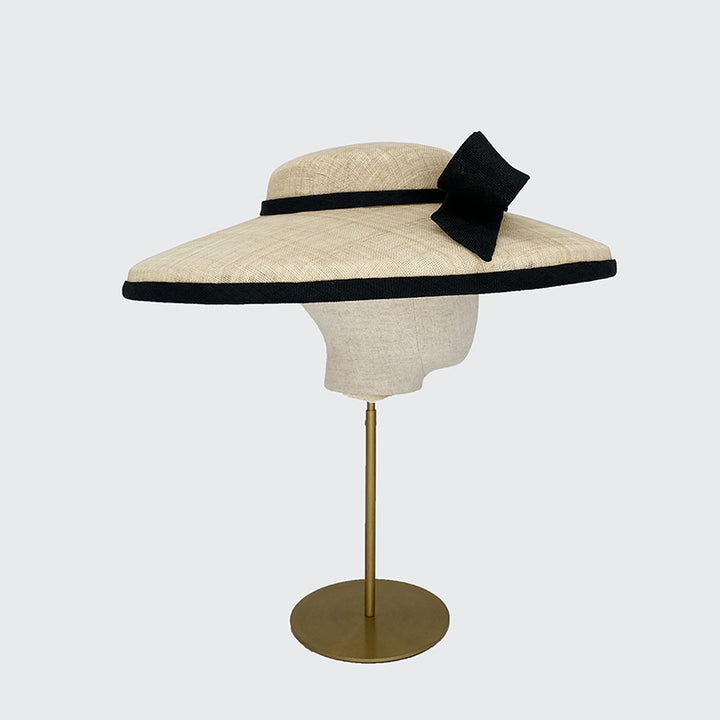 Side view of a natural fine straw cut through with a black edge and a black bow on a linen display head