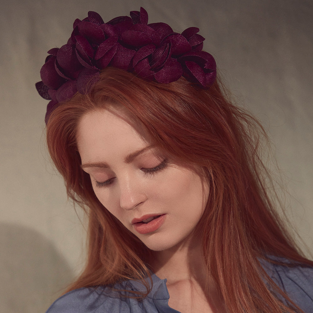 Woman with red hair wearing a blue blouse and a purple fine straw petal headband