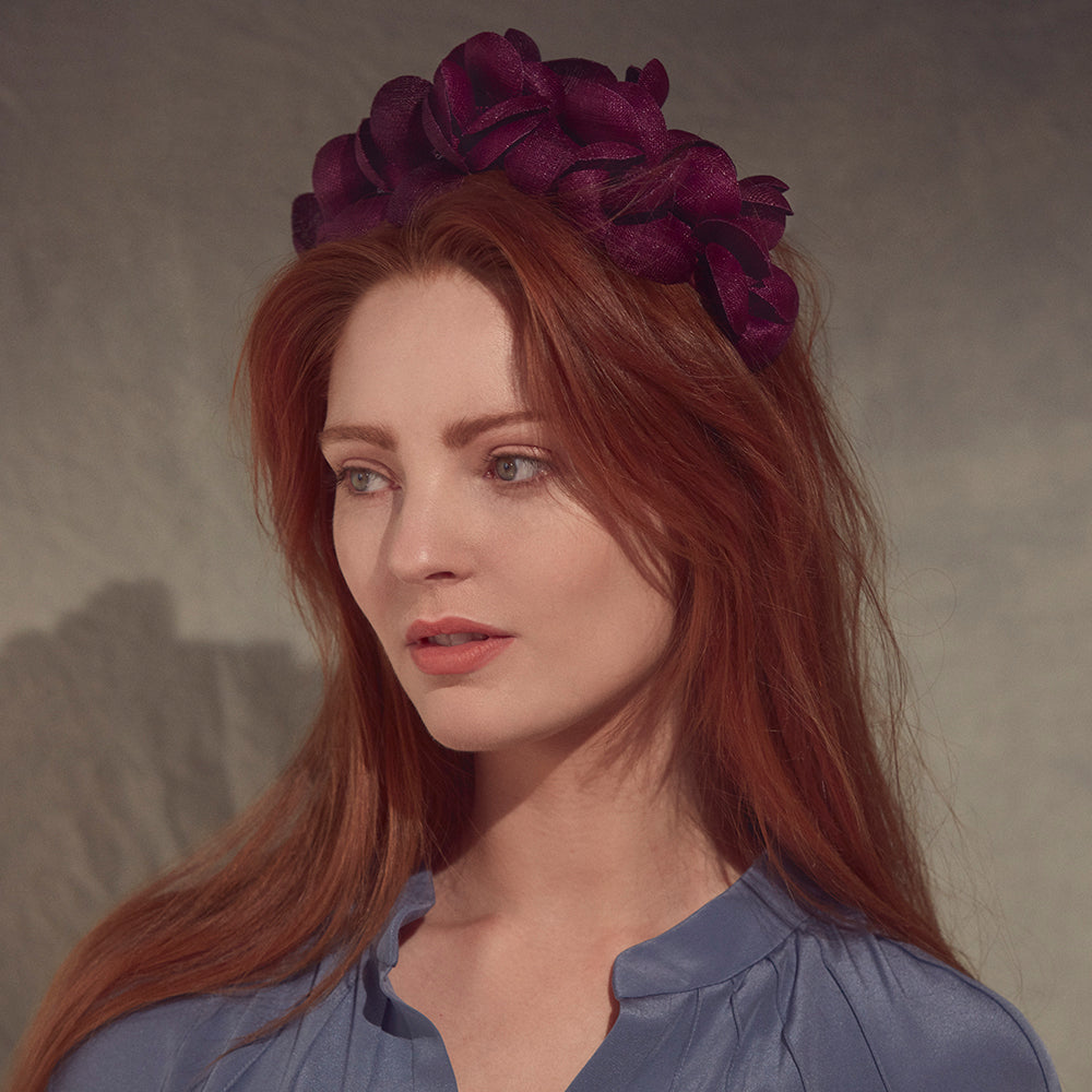 Woman with red hair wearing a blue blouse and a purple fine straw petal headband