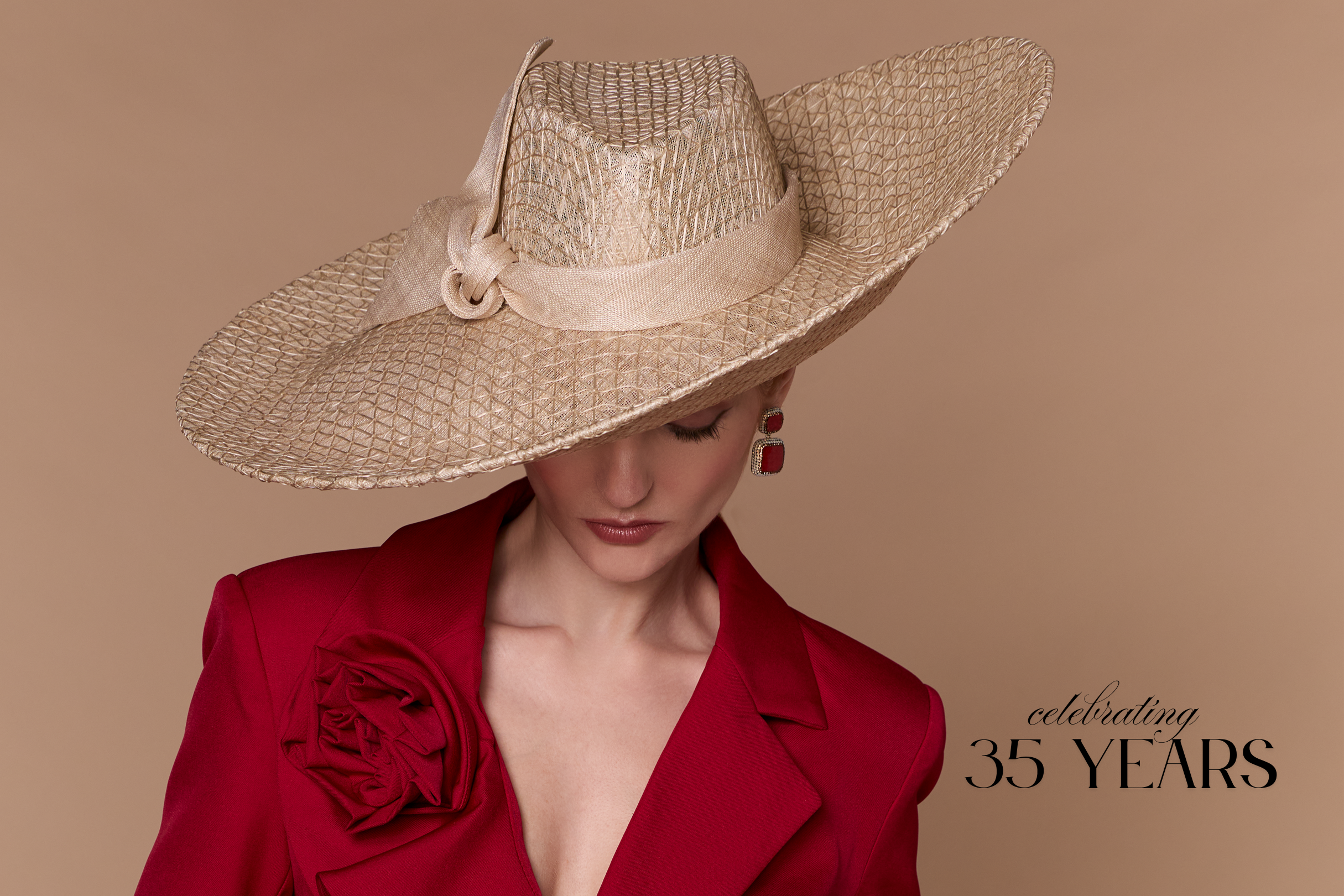 Woman wearing a large straw hat and red jacket on a beige background with text 'celebrating 35 years'.