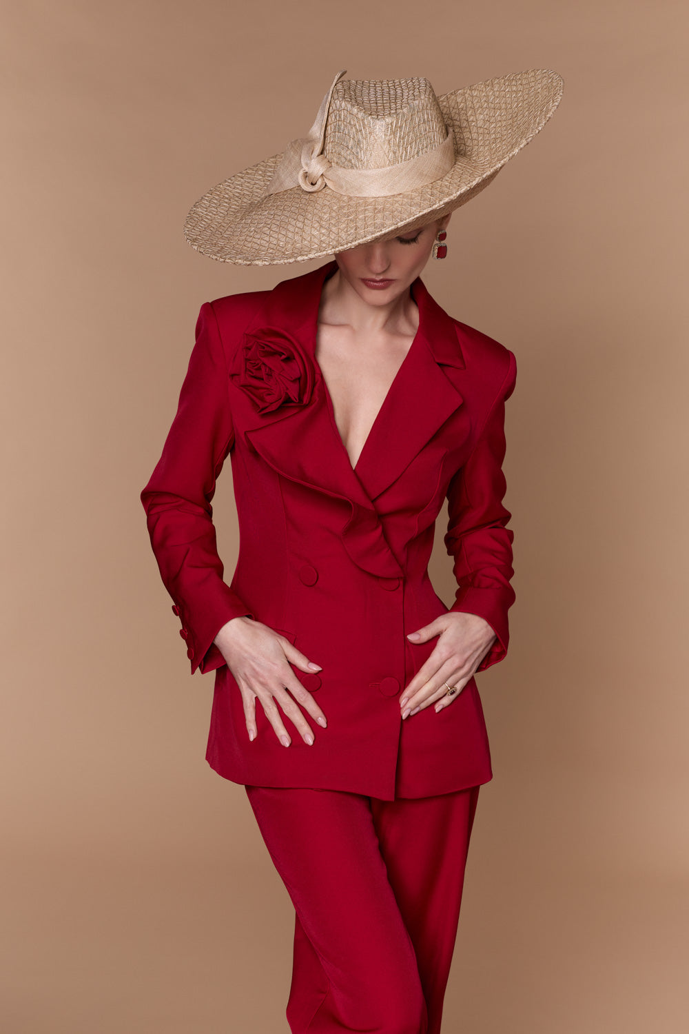 Woman wearing a red suit with a large straw fedora on a beige background
