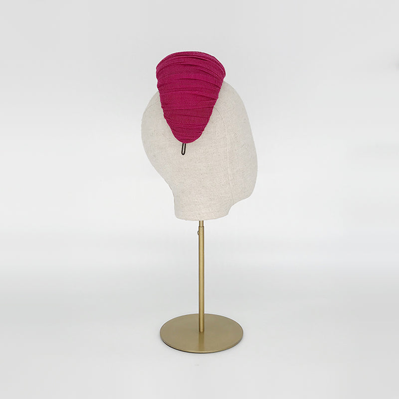 Side view of a pink pleated silk straw crescent on a linen display head