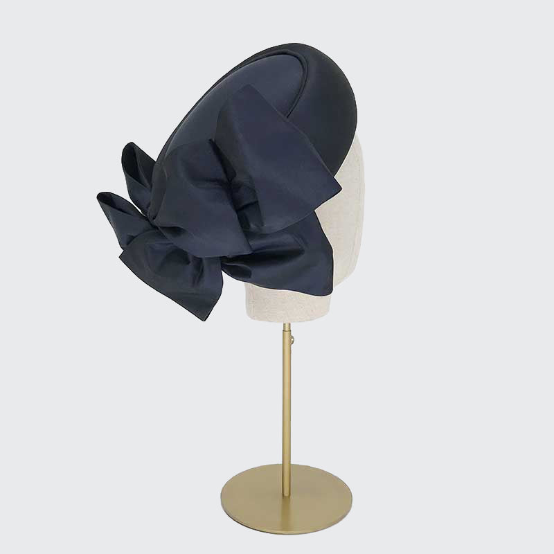 Side view of a navy taffeta silk Jackie O pillbox with bows on a linen display head