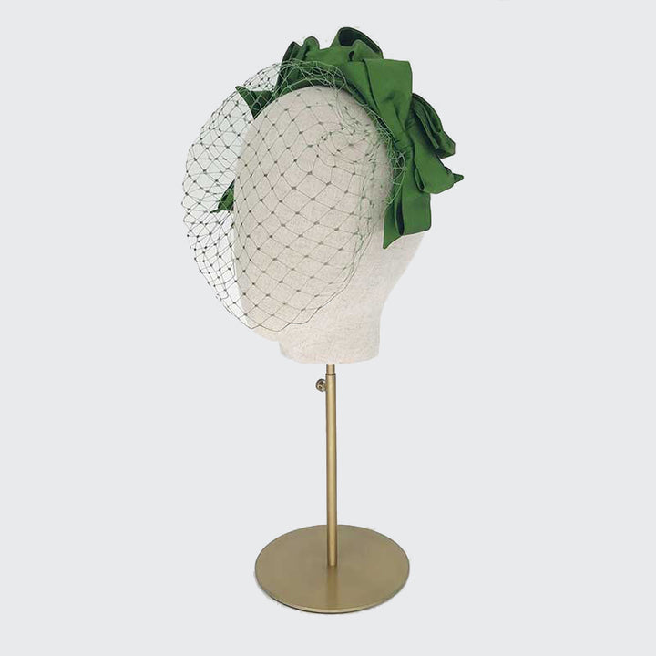 Side view of a green silk bow headband with face veil on a linen display head