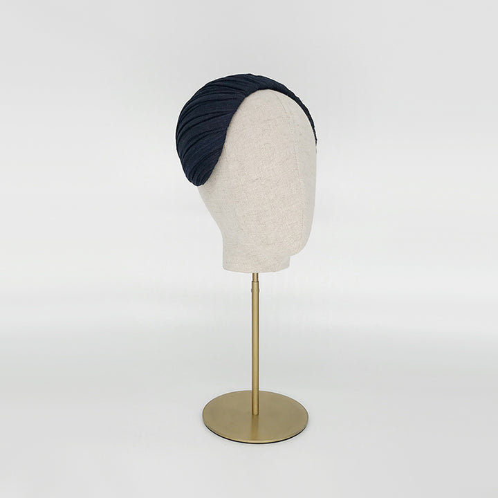 Side view of a navy pleated silk straw headpiece on a linen display head