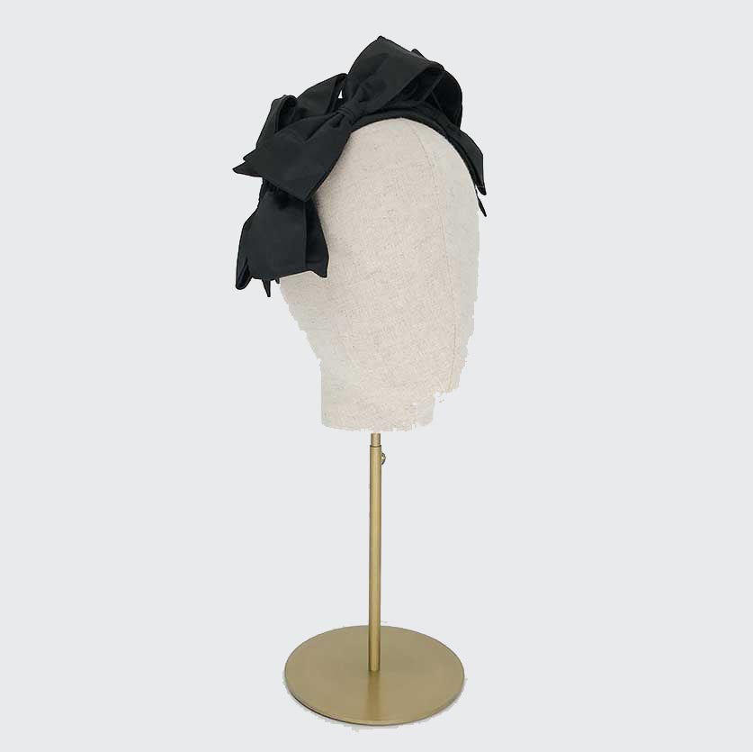 Side view of a black silk bow headband on a linen display head