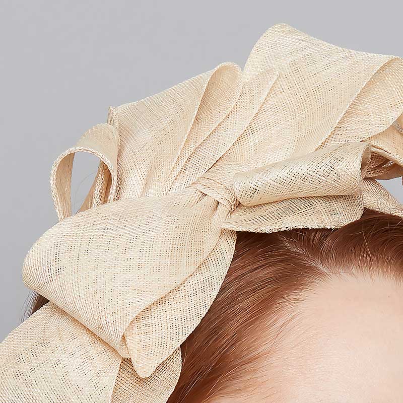 Close up of a natural fine straw bow headband on a linen display head