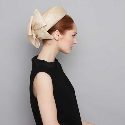 Woman with red hair wearing a black dress and a natural fine straw Jackie O pillbox with bows