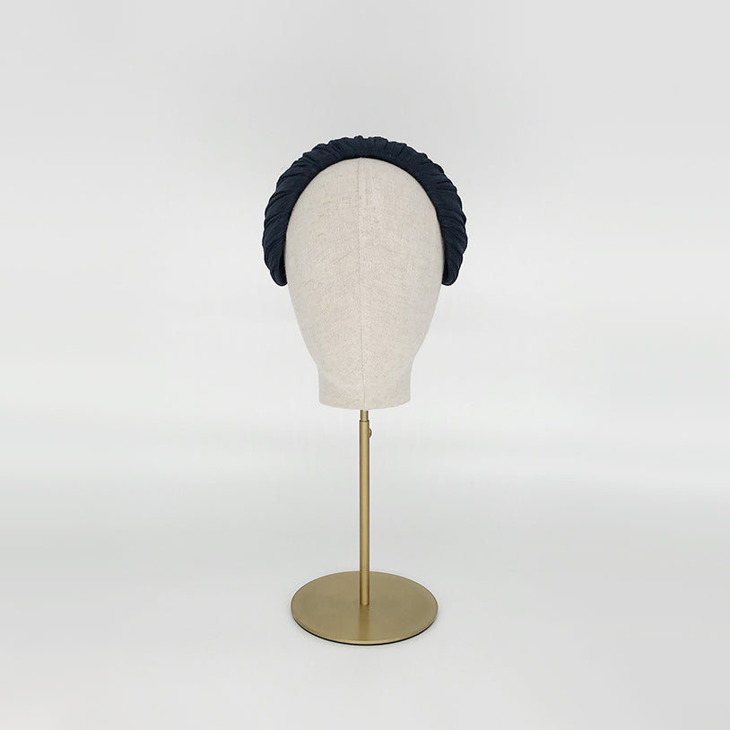 Photo of a navy pleated silk straw headpiece on a linen display head