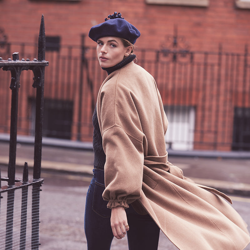 Woman wearing a camel coat and a navy wool beret with a ribbon pom
