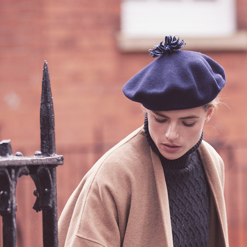 Woman wearing a camel coat and a navy wool beret with a ribbon pom