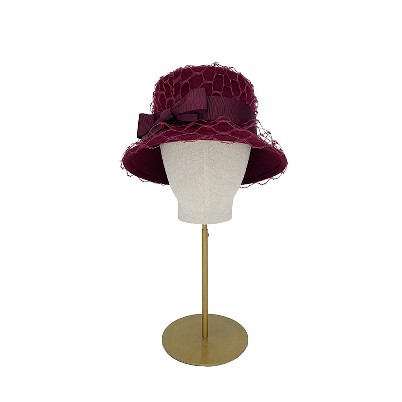 Photo of a burgundy bucket hat trimmed with veiling and a bow on a linen display head