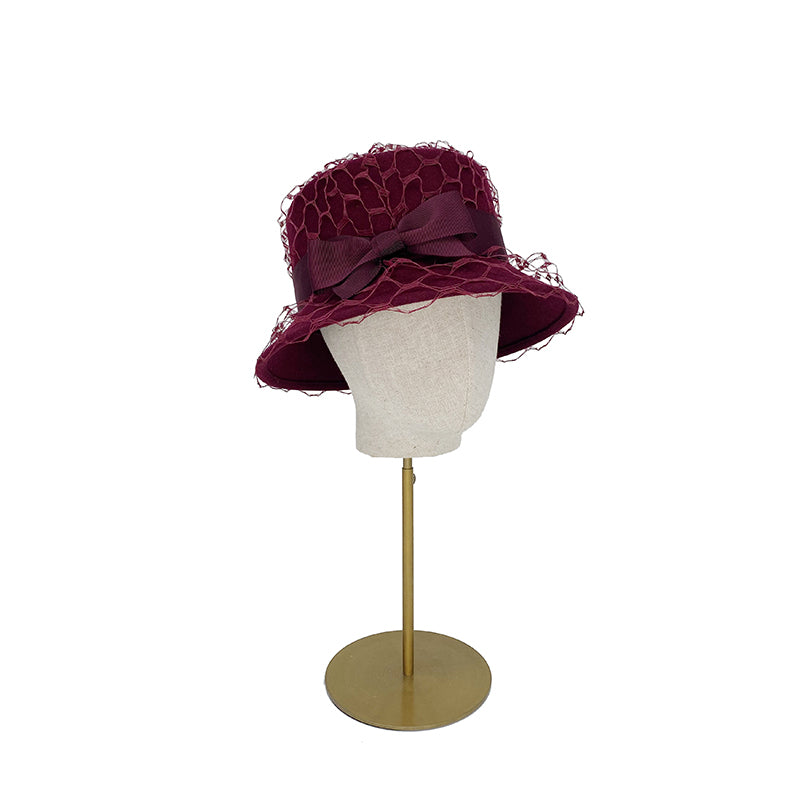 Side view of a burgundy bucket hat trimmed with veiling and a bow on a linen display head