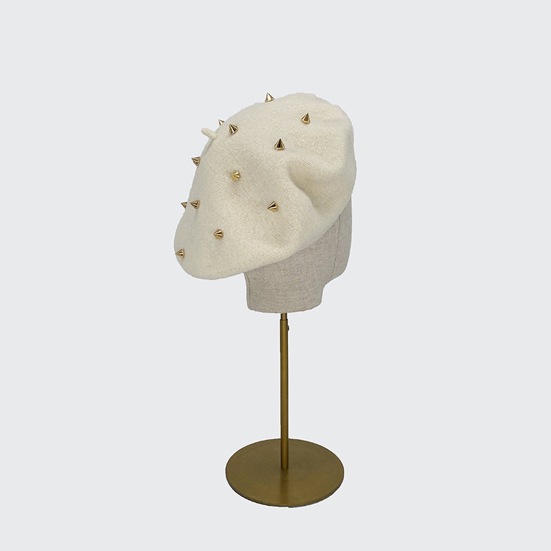 Photo of white wool beret with gold studs on a linen display head