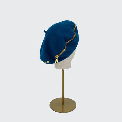 Photo of teal wool beret with gold zip on a linen display head