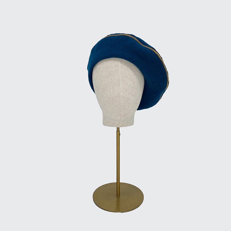 Photo of teal wool beret with gold zip on a linen display head