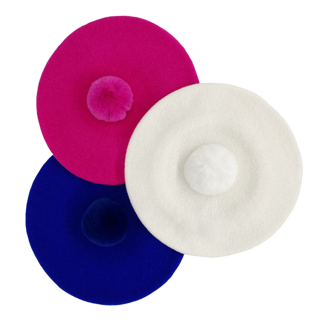 Photo of three berets with fur poms in royal blue, hot pink and white