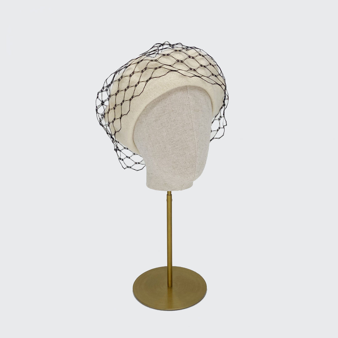 Photo of a cream wool beret with black veiling on a linen display head