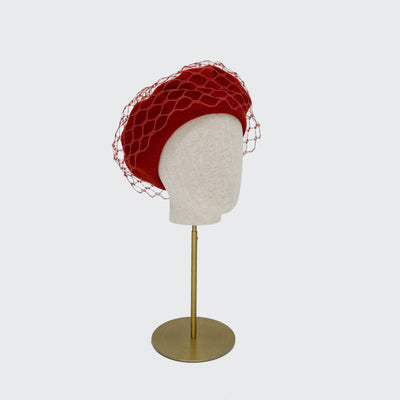Photo of a burnt orange wool beret with orange veiling on a linen display head