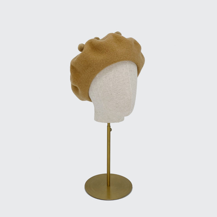 Photo of a camel wool beret with camel pom poms on a linen display head
