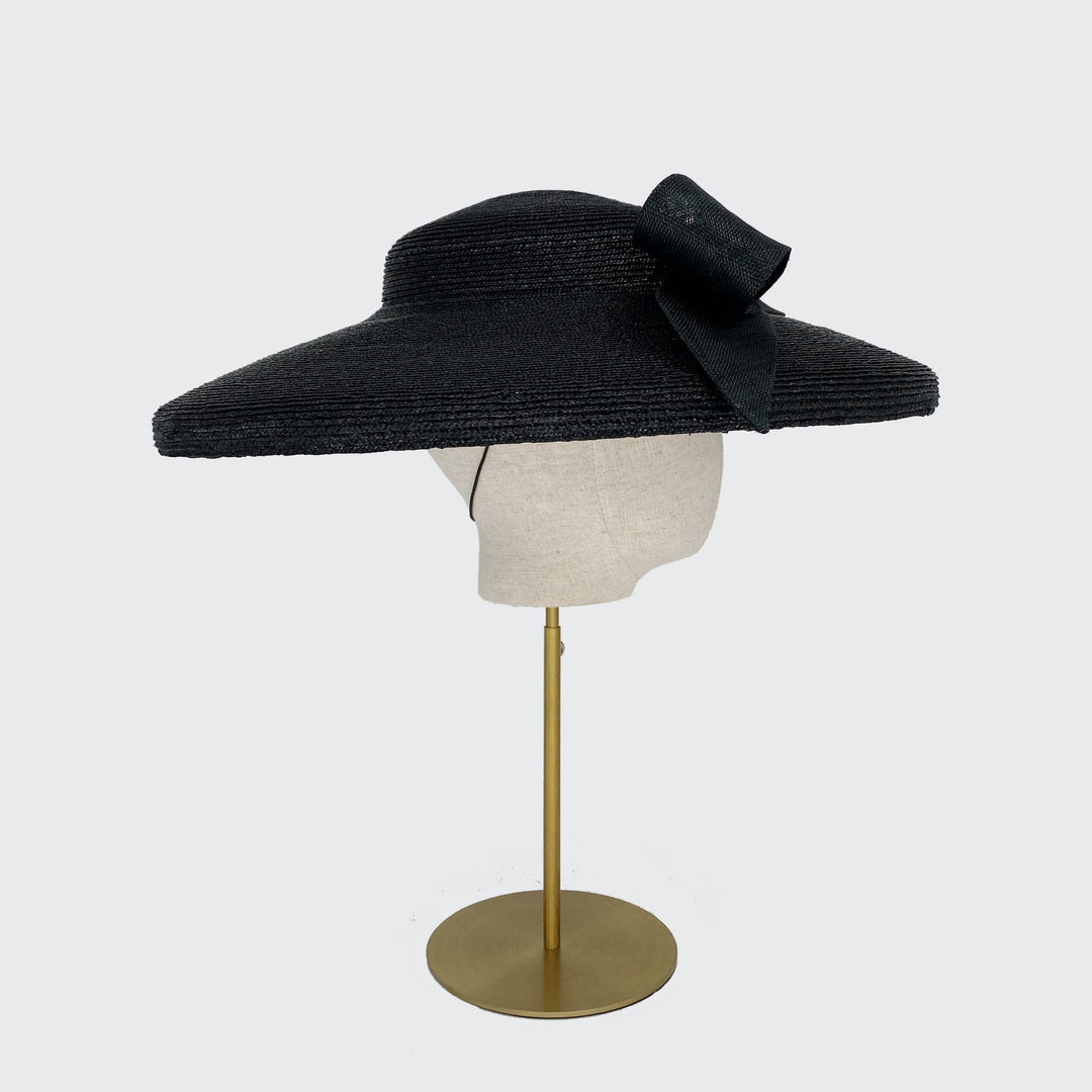 Side view of a black Italian straw cut through with a black bow on a linen head
