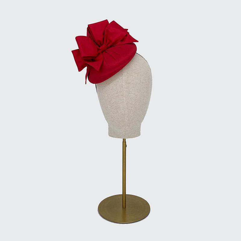 Photo of a red silk pillbox with bows on a linen display head