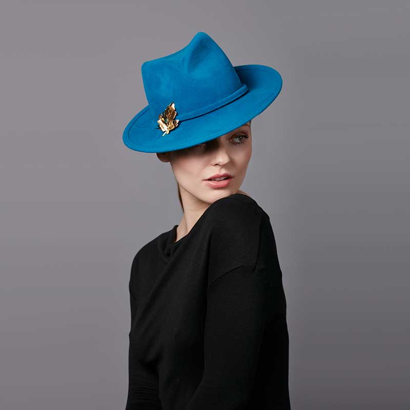 Woman wearing a black top and a turquoise velour felt trilby with a gold leaf