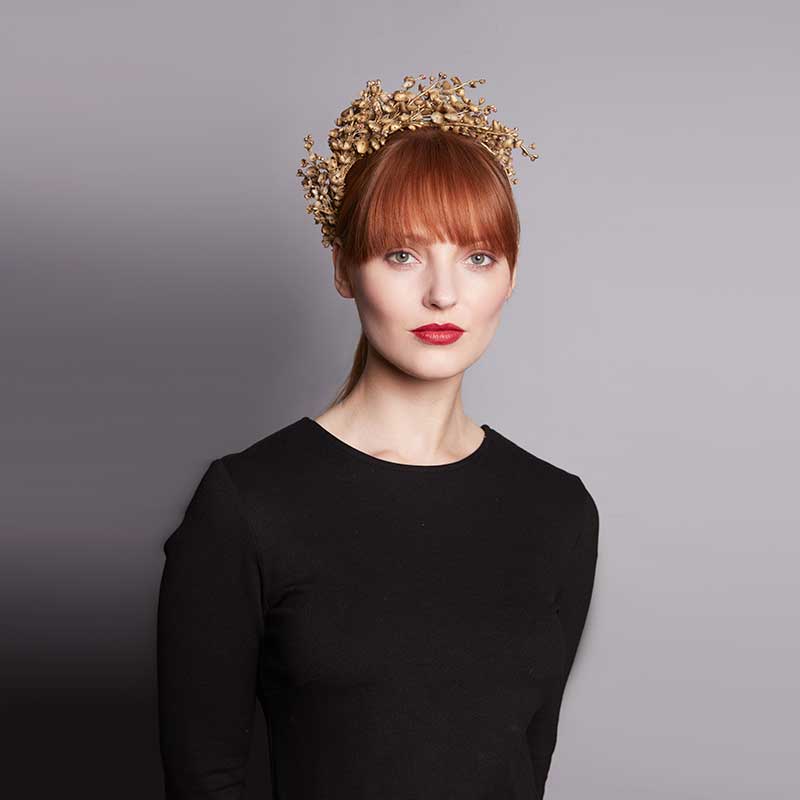 Woman with red hair wearing a black dress and a gold Lily of the Valley headdress