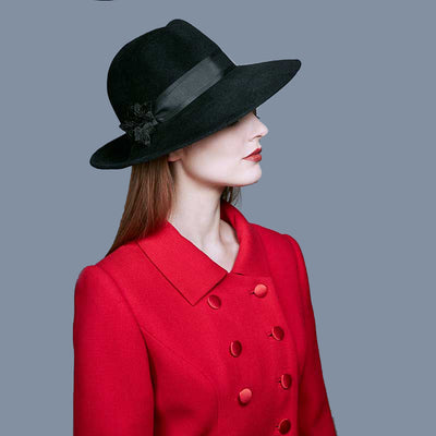 Woman wearing a red coat and a balck velour felt fedora with black velvet leaves