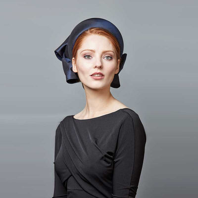 Woman with red hair wearing a black dress and a navy taffeta silk Jackie O pillbox with bows